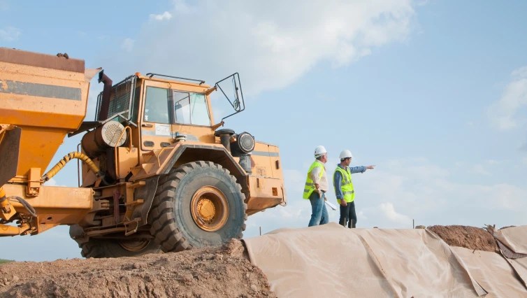 two construction workers on job site with dump truck next to them