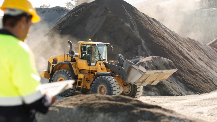 front loader on construction site carrying dirt with worker in the foreground