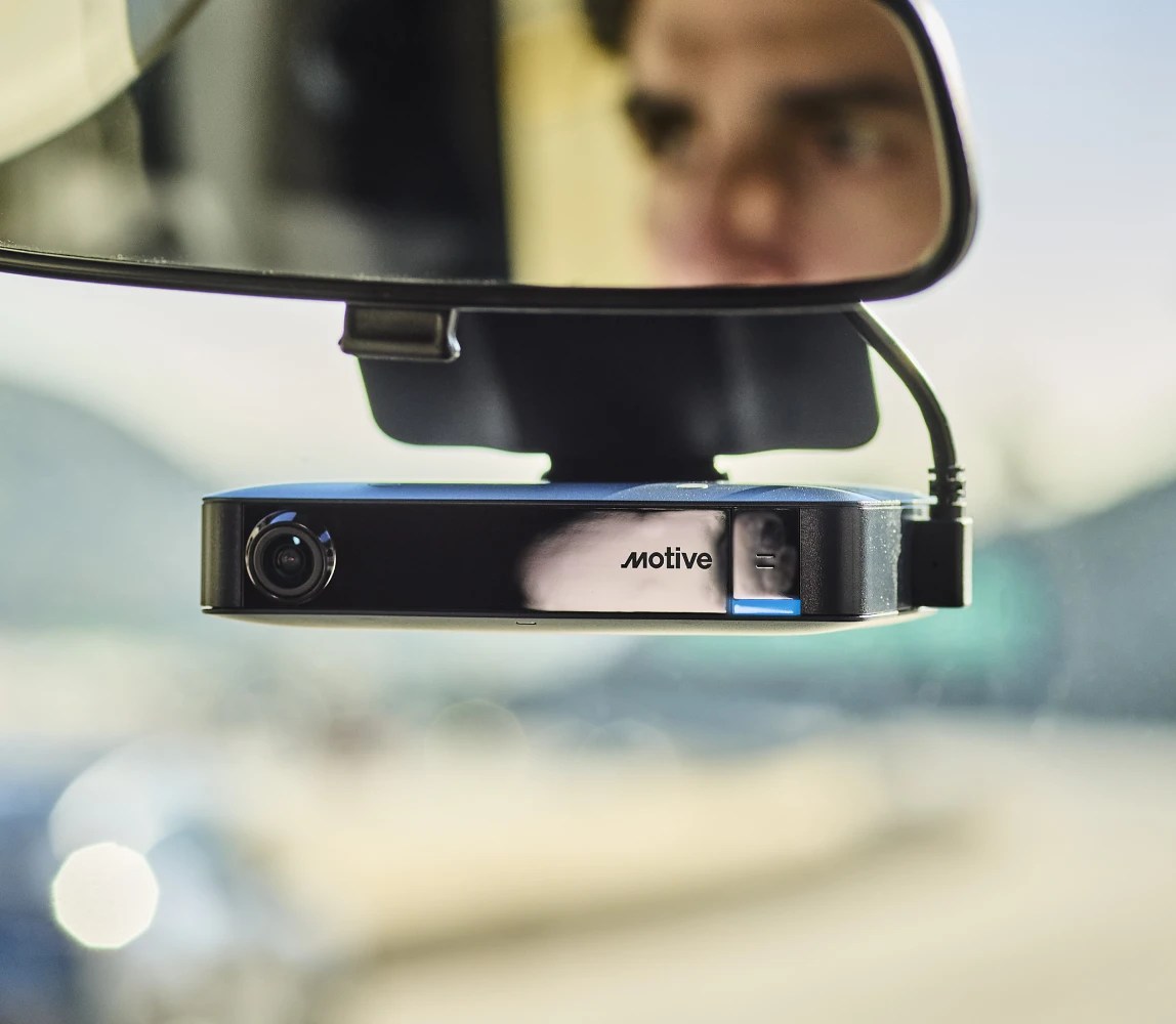 Motive AI dashcam plus mounted on a vehicle windshield with a driver visible in the rear view mirror